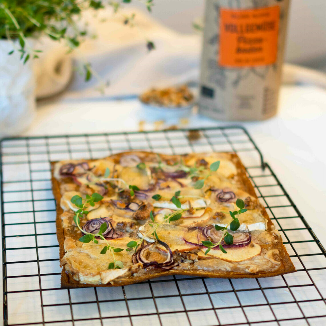 gebackener Pizzaboden als Flammkuchen auf Gitter, belegt mit Äpfeln, Zwiebeln, Camembert, Walnüssen und Thymian